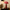 Red vase with pink flowers on a nightstand next to a white alarm clock and books.