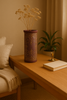 Decorative vase with dried flowers on a wooden table in a warm-toned room.